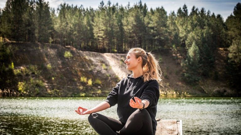 Serene moment of a woman practicing meditation near a forest lake in Lithuania.